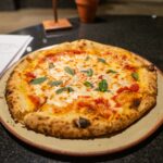Freshly baked Margherita pizza with basil and mozzarella, served on a stone counter.